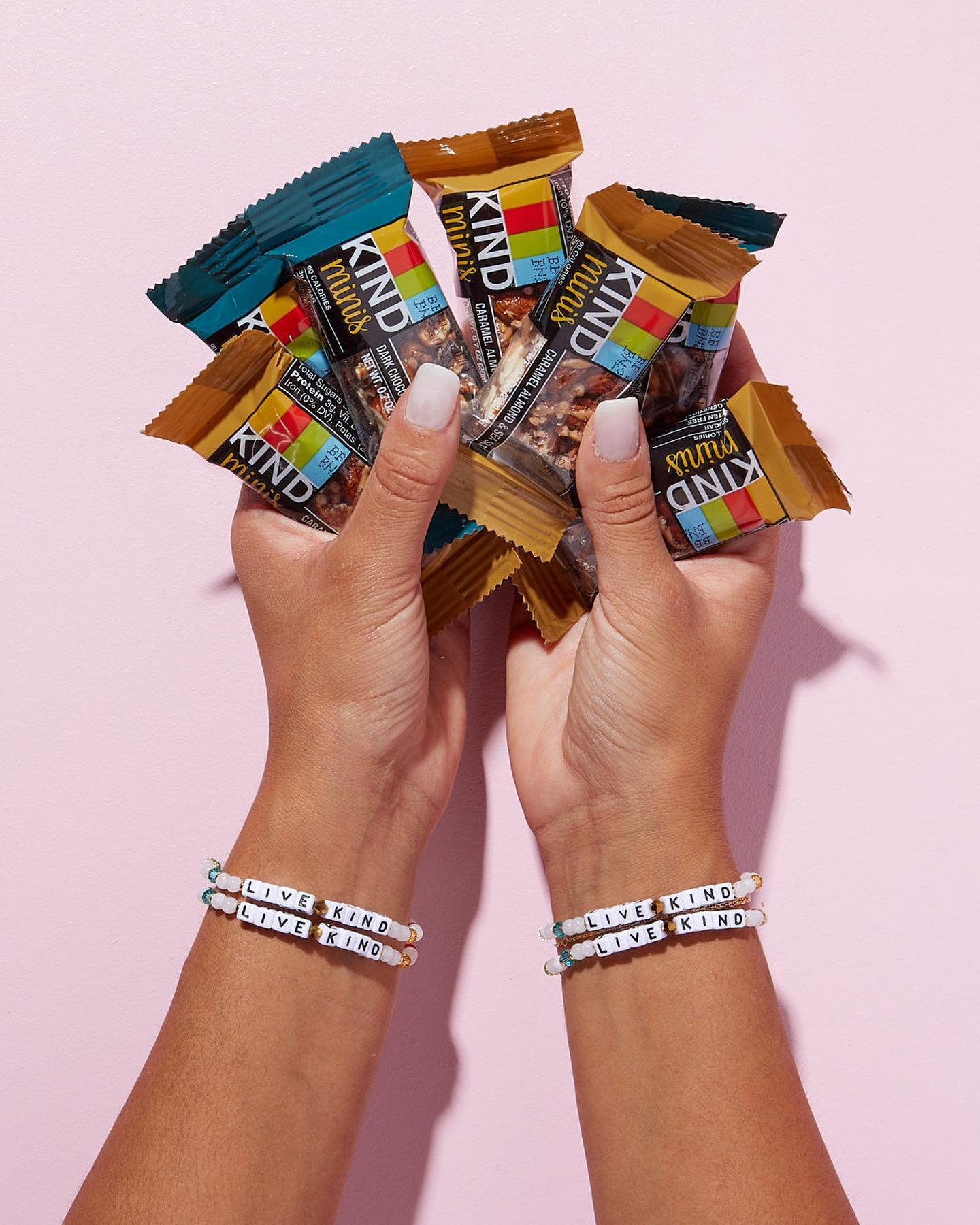 Hands holding KIND Minis with Live KIND bracelets